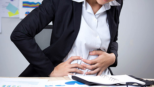 A woman in pain because of Chron's Disease at her desk.