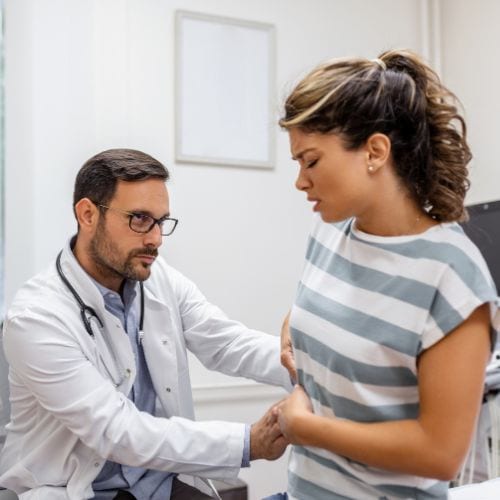 A doctor examining a female patient's abdomen in a medical office.