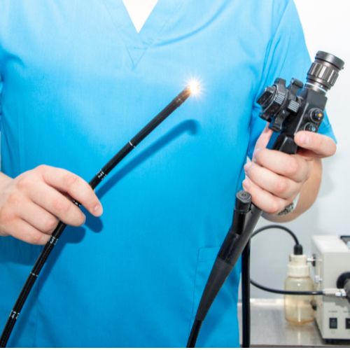 Medical professional in blue scrubs holding an endoscope with a light on the end.