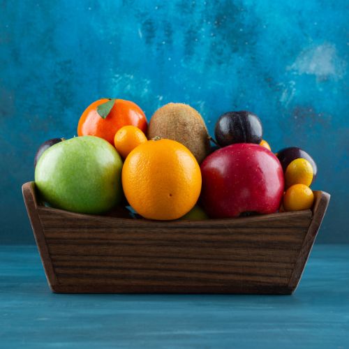 A wooden bowl filled with assorted fresh fruits on a blue background.