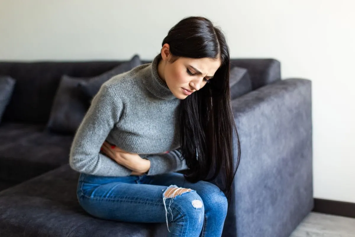 Gastritis Woman sitting on a couch, clutching her abdomen in pain.