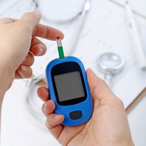 Close-up of hands holding a blue glucose meter with a test strip inserted.