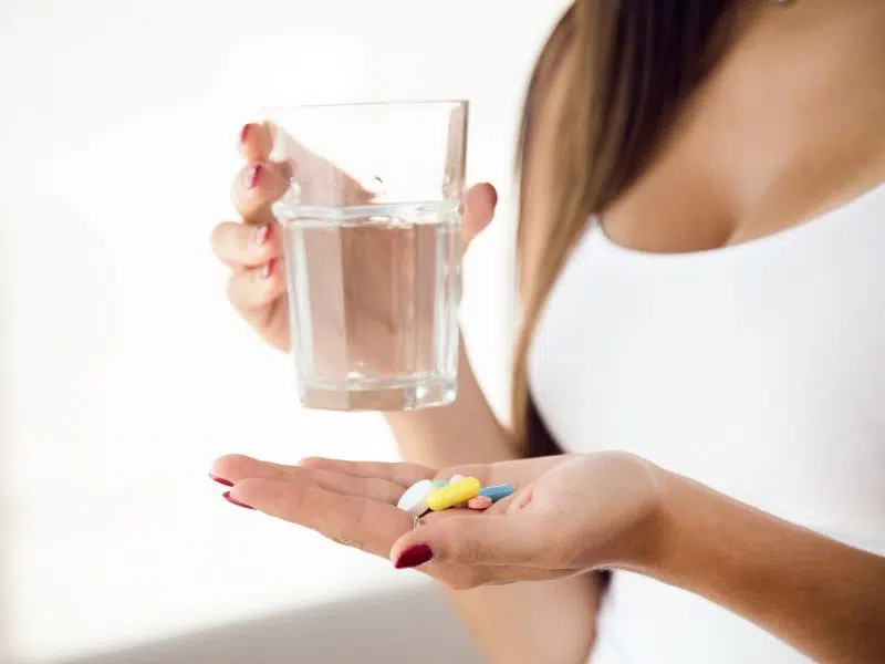 Woman holding a glass of water and various pills in her hand.